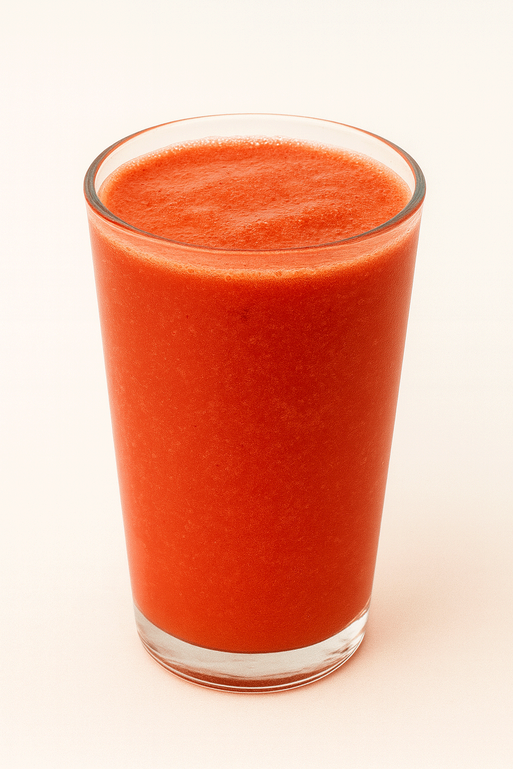 A tall, transparent glass filled with red-orange juice made from orange, carrot, and beet, placed against a light background.